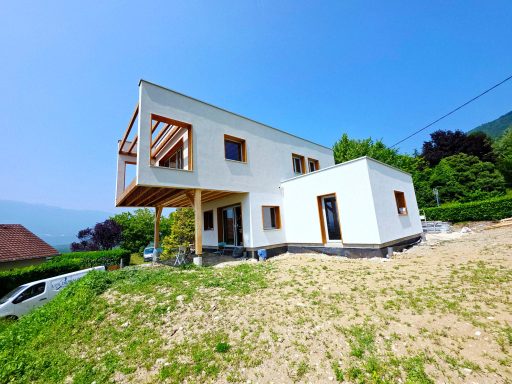 enduit sur fibre de bois Maison moderne à deux niveaux, avec un balcon et un jardin verdoyant, sous un ciel bleu.
